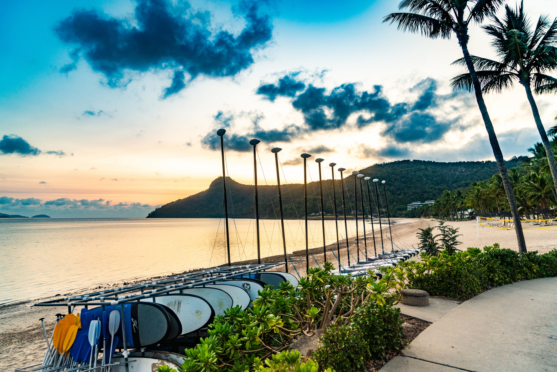 Kayaks and catamarans lined up on the sand at sunrise beside a tropical Australian island beach resort
