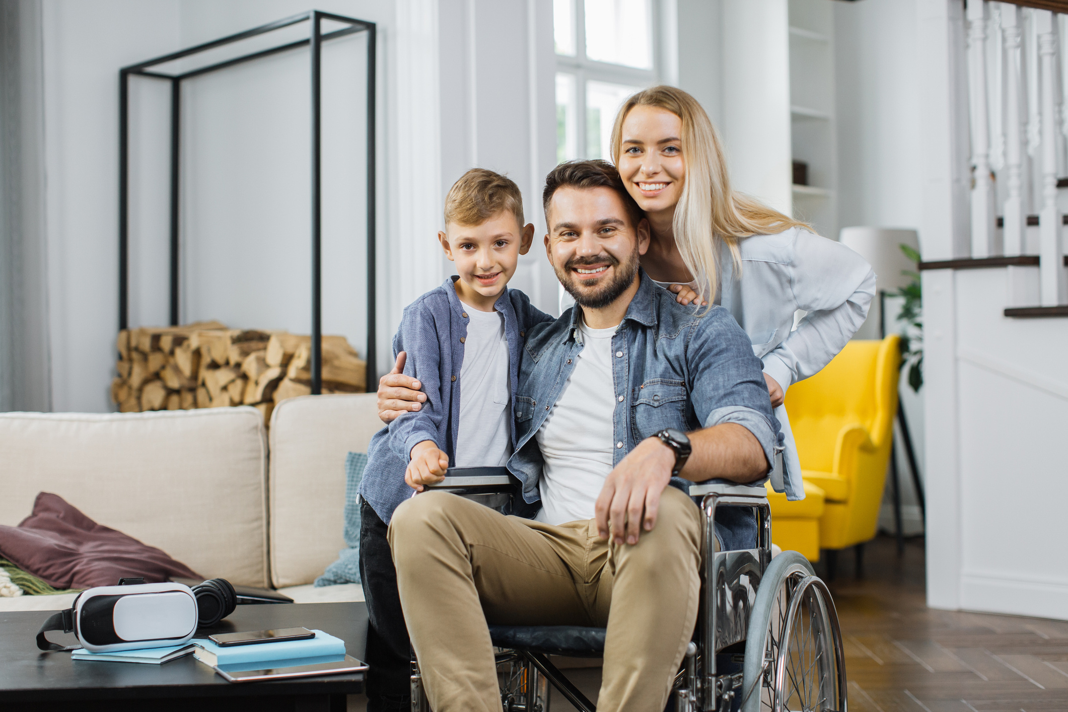 Smiling family at home with a man using a wheelchair in a bright, open-plan living room