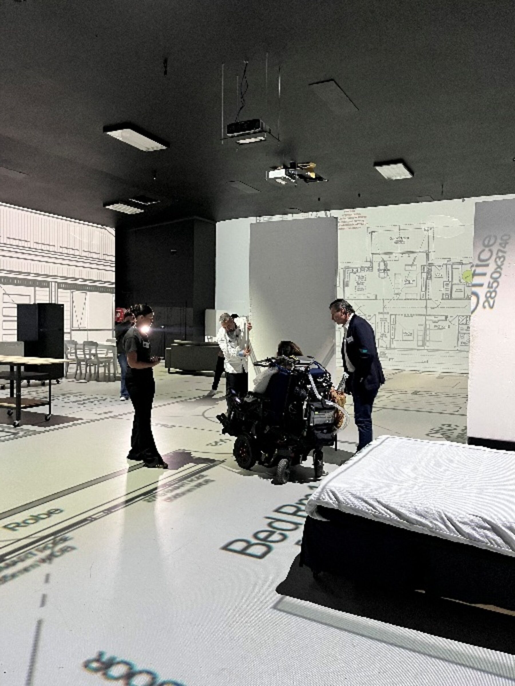 A participant and support team testing bedroom, robe and office dimensions on a 1:1 projected SDA floor plan at Lifesize Plans Burwood