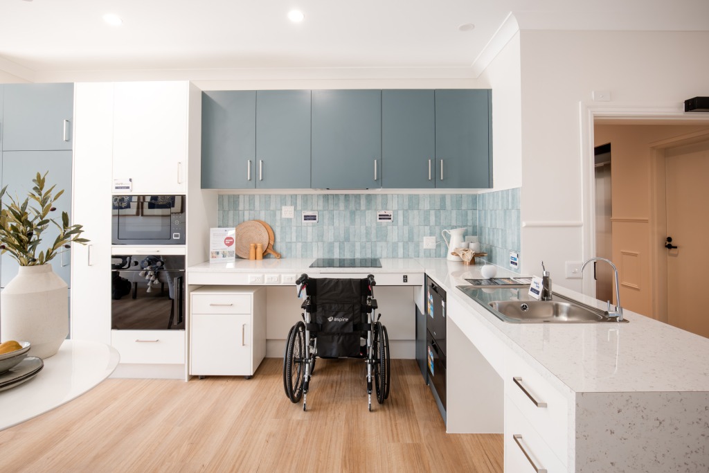 Accessible kitchen in a PNP home with a lowered benchtop, wall oven and a wheelchair positioned at the workspace