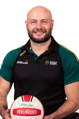 Chris Bond OAM, captain of the Australian Steelers wheelchair rugby team, in his green and gold team polo holding a rugby ball.
