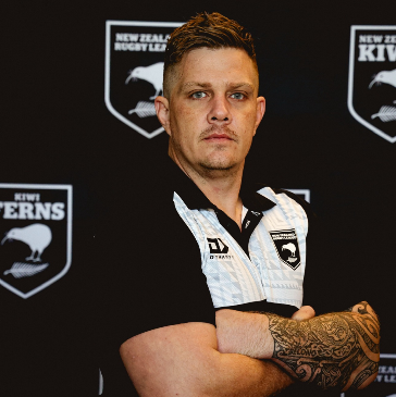Dan Scott, wheelchair rugby league and wheelchair AFL athlete, with arms folded in front of a New Zealand Rugby League backdrop.