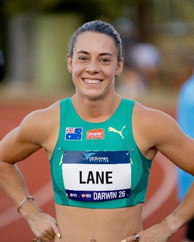 Ebony Lane, Australian Olympic sprinter, smiling in her green and gold Australia athletics uniform on the track.