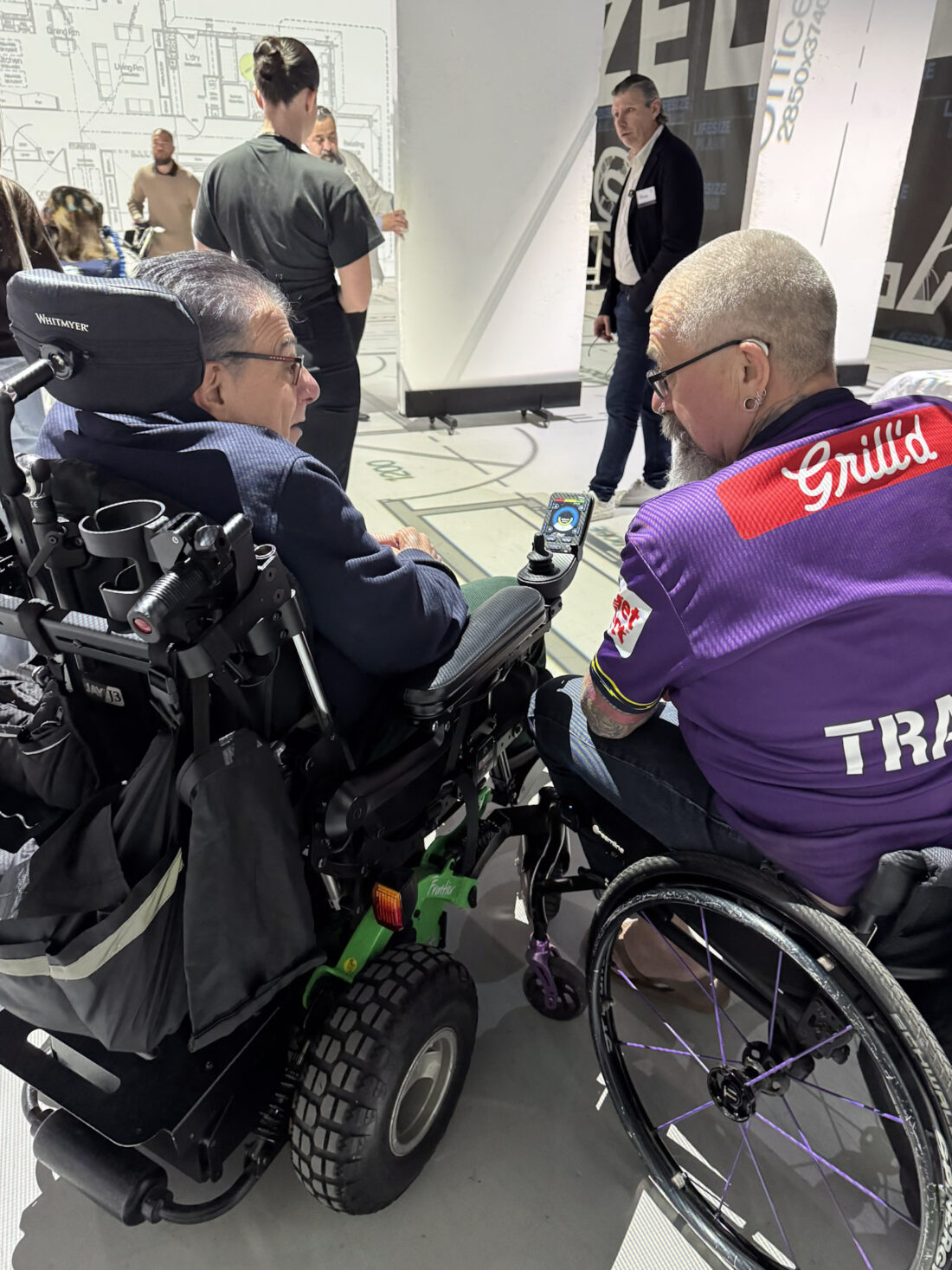Two wheelchair users in conversation beside the full-scale projected floor plan during the Macquarie Fields SDA walkthrough