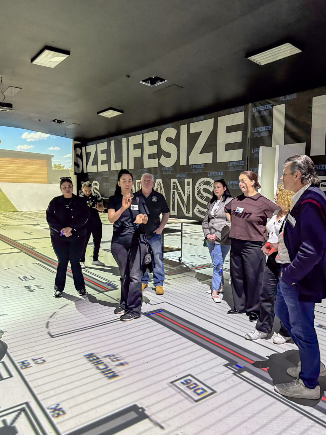 A Lifesize Plans guide briefing the Macquarie Fields project group as they stand on the full-scale projected floor plan