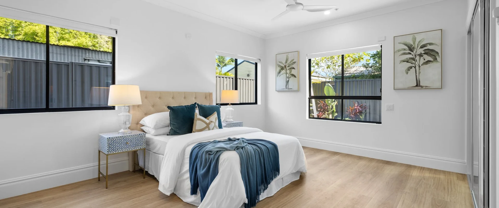 Light-filled SDA bedroom with queen bed, twin bedside lamps, ceiling fan and wide timber-look flooring for wheelchair access